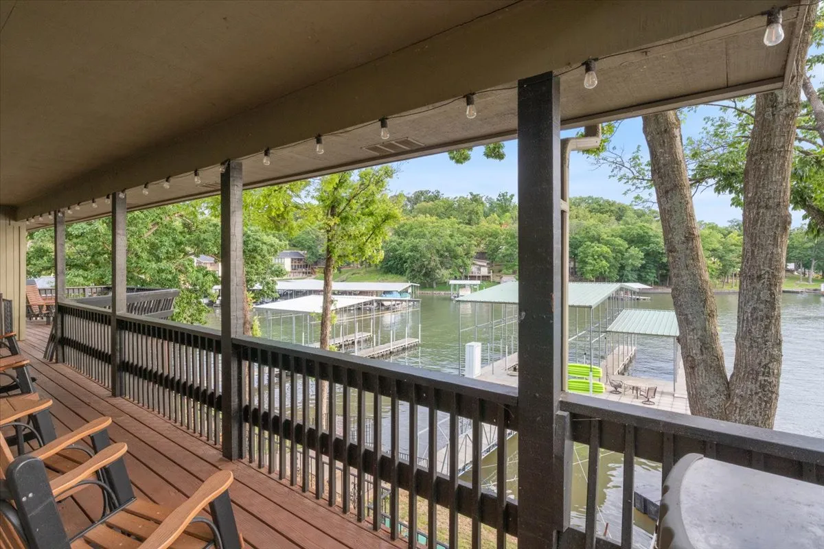 A spacious wooden deck overlooking the tranquil lake, furnished with lawn chairs and adorned with hanging string lights. The view encompasses serene water, lush greenery, and a welcoming setting perfect for relaxation or social gatherings.