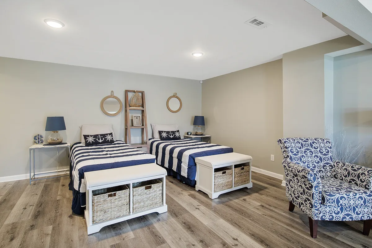 A playful bedroom with twin beds dressed in navy and white stripes, complemented by blue accent lamps and a patterned chair. The space feels welcoming and practical for families or friends traveling together.