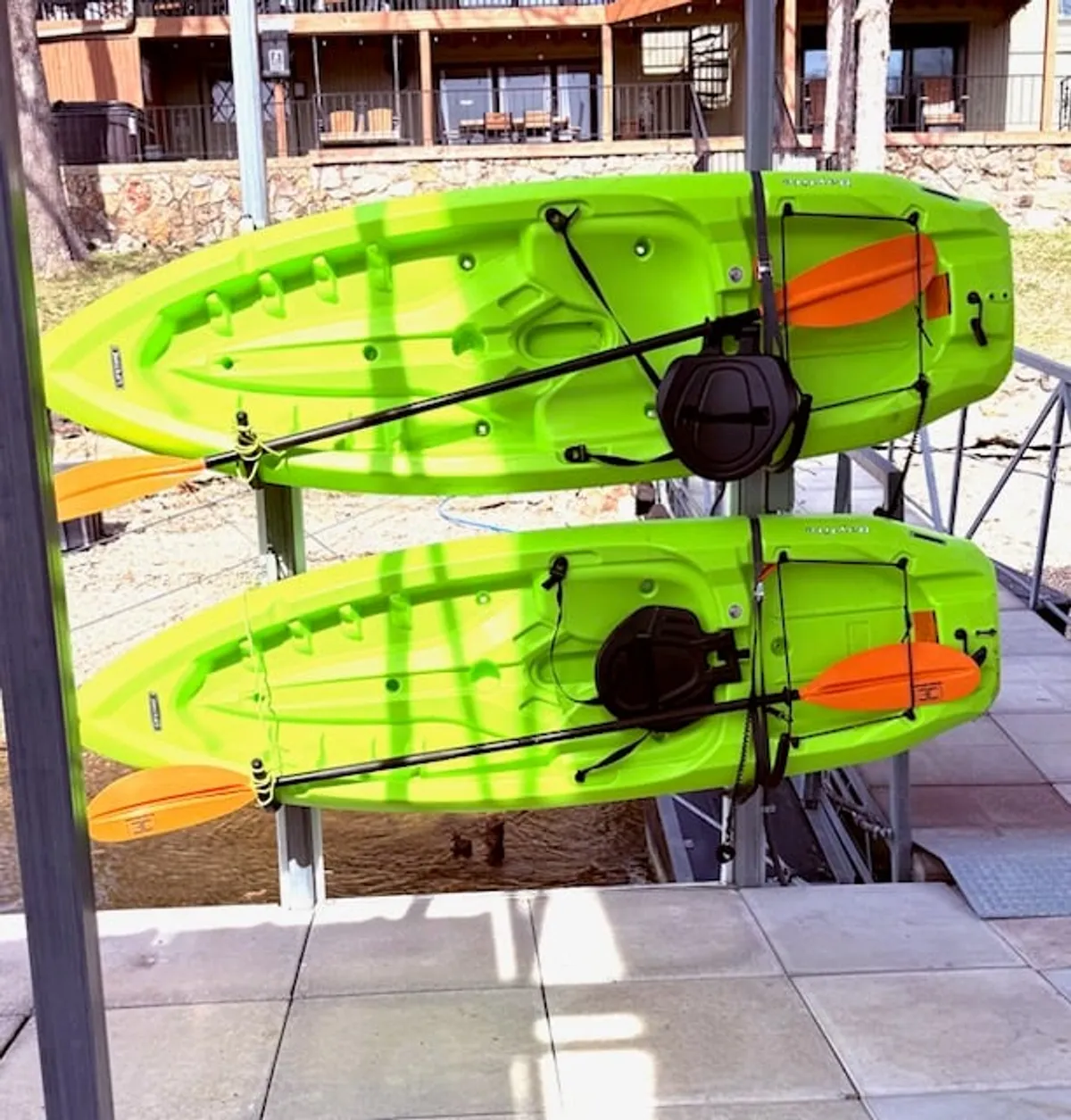 Bright green kayaks with orange paddles rest near a wooden balcony—ready for guests to explore the water. The scene blends the thrill of water sports with the convenience of direct lake access.