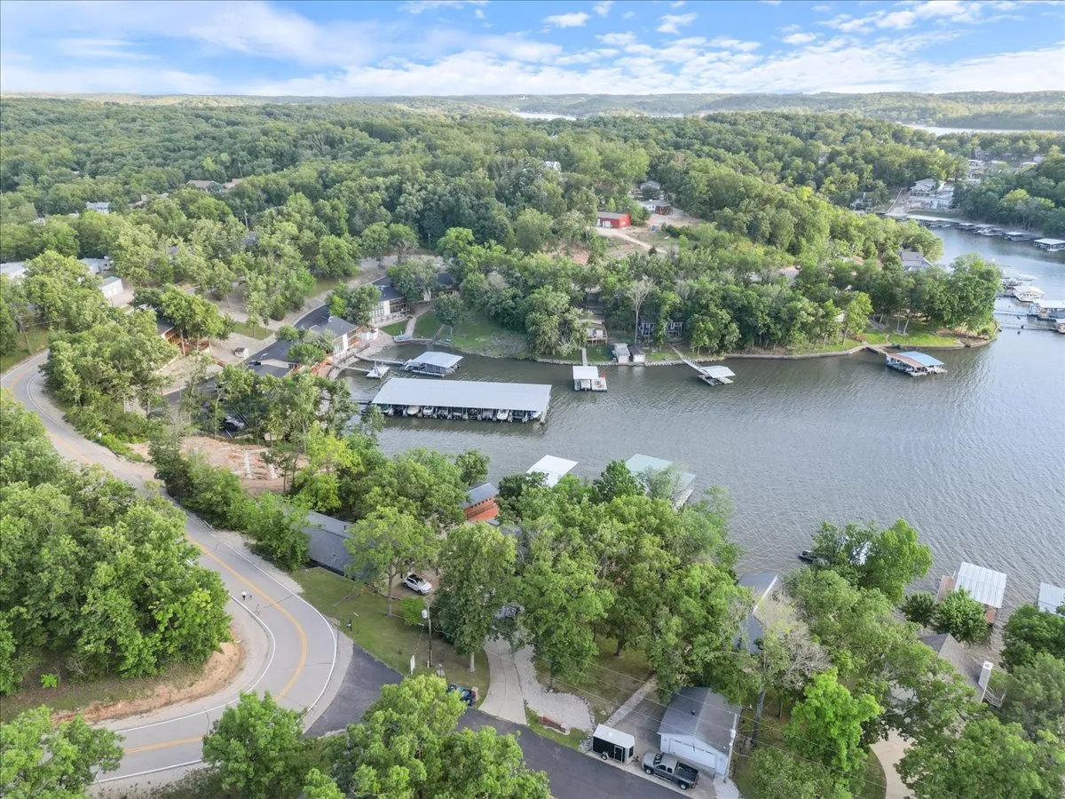 A sweeping aerial view captures lush greenery, winding roads, waterfront docks, and homes nestled amongst the trees, highlighting the area's natural beauty and proximity to water-based adventures.
