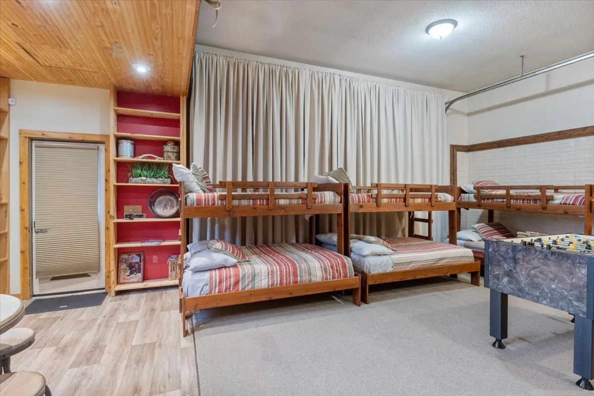A fun, bunkhouse-style bedroom with bunk beds and a game table, surrounded by wooden shelving. The mood is playful and relaxed, ideal for children’s sleepovers or group gatherings.