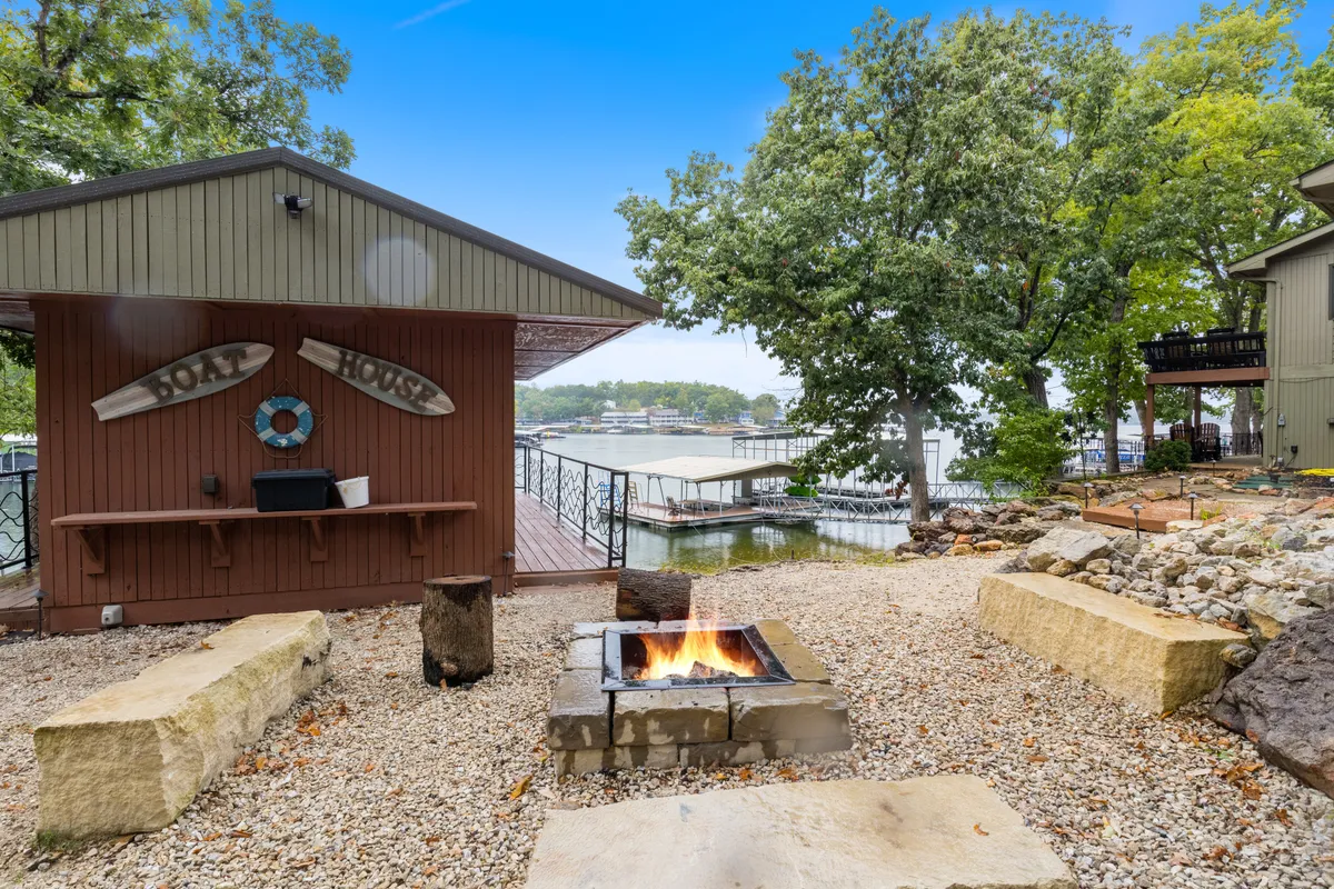 This exterior image features a cozy fire pit with seating overlooking the lake, a dock, and a soak house, all set against a serene waterfront backdrop. The setting encourages campfire gatherings, marshmallow roasting, and sunset views—extending the communal experience to the outdoors.