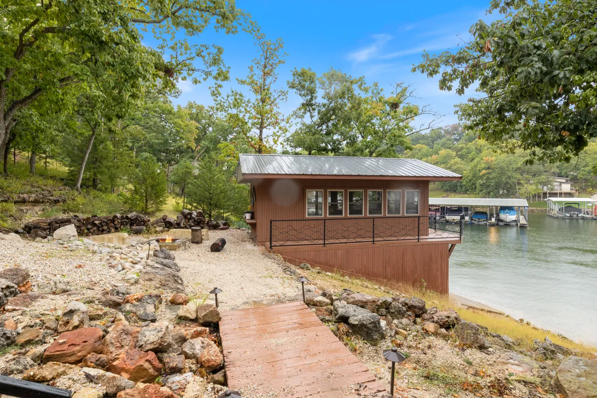 A peaceful lakeside scene with a wooden pathway, outdoor seating, and exterior view of the building surrounded by trees. The image invites relaxation and suggests direct access to nature.