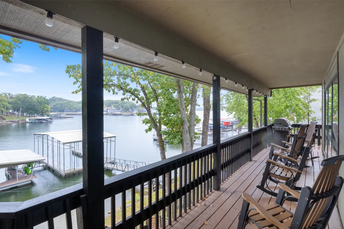 A serene lakeside dock extends out over calm water, with rocking chairs positioned for relaxation, surrounded by trees. The scene is peaceful, ideal for fishing, launching kayaks, and enjoying the view—matching the private dock features described.