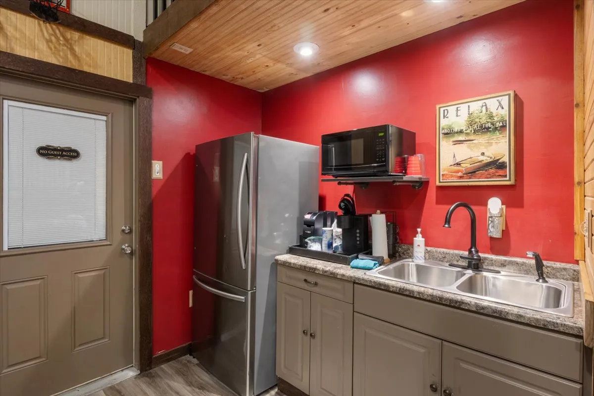 A compact kitchenette area with a refrigerator, kitchen sink, microwave, and a decorative art piece. The setup is practical and welcoming, ideal for preparing snacks and light meals without leaving the bunkhouse.