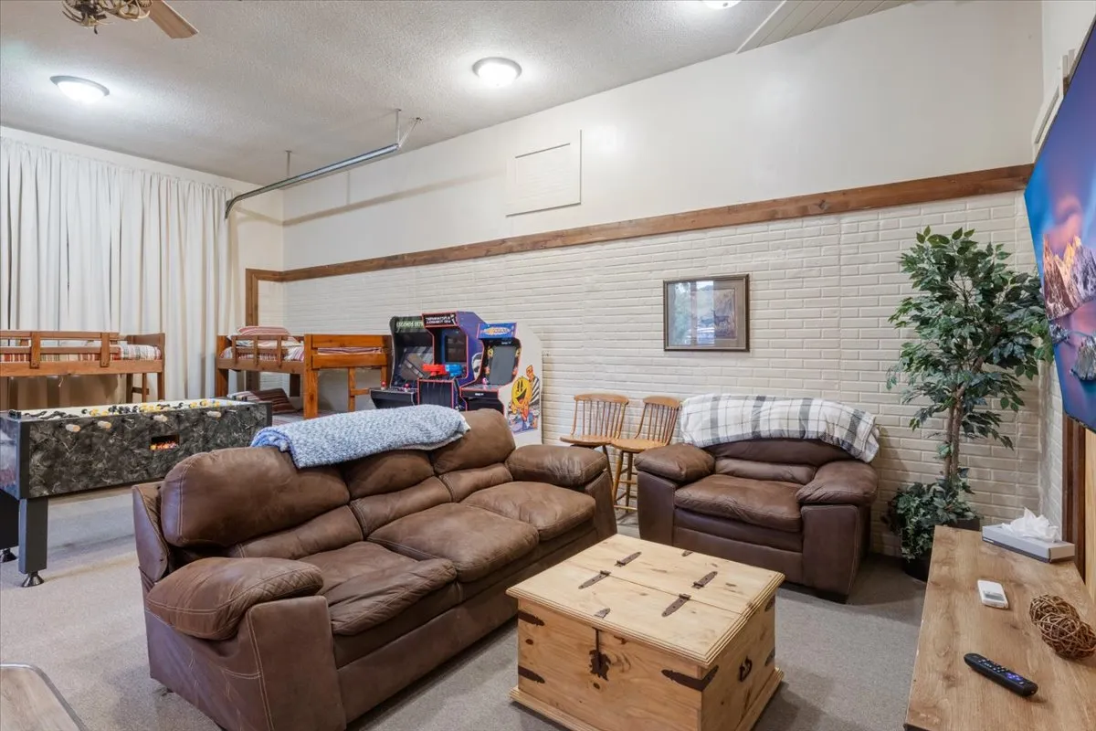 An inviting game room setup featuring comfortable couches, a wooden coffee table, arcade machines, and bunk beds. The layout encourages social gatherings and late-night fun, with a cozy, relaxed mood perfect for groups.